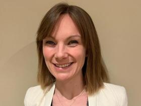 A smiling woman with shoulder-length brown hair wearing a cream jacket