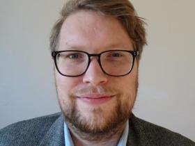 A man with short brown hair and dark rimmed glasses