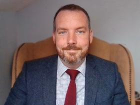 Photo of Dr David Campbell, wearing a dark suit and red tie
