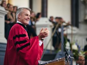 Professor Stephen Blyth in a red academic gown speaking in the Sheldonian