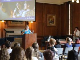 A woman in a bright blue t-shirt gives a talk to a room full of students