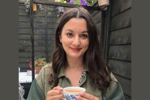 A woman with long dark brown hair sitting in a garden with a cup of tea
