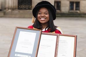 Vee Kativhu wearing academic robes holding up her three degree certificates