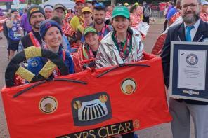 A photo of runners at the London marathon in a 10-person red bus costume being awarded a Guinness World Record certificate