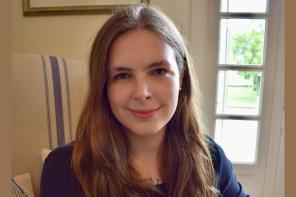 Dr Grace Mallon, a woman with long brown hair, sits in a light-filled room