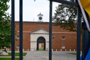 A red brick building seen through some black iron gates covered in bright blue and yellow bunting