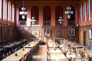 A view of the inside of the LMH dining hall, which has deep pinky red walls, wooden panelling and light streaming through the high windows