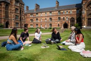 Students sitting on the grass outside some tall red brick buildings
