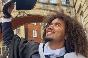 Ras.I Martin, who wears a black and white graduation gown, standing underneath the Hertford College bridge in Oxford