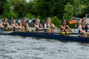 Women wearing blue and white lycra rowing suits sitting in a boat and rowing in Oxford's summer eights competition on the River
