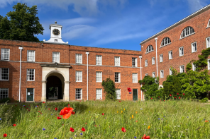 A red brick building with a clock tower set against a bright blue sky and with grass and red poppies in the foreground