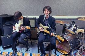 Photo of two young men with guitars sitting in a music studio space about to perform