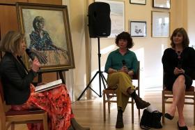 Three women sit in front of a portrait of Professor Christine Gerrard