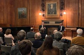 zahaan bharmal and todd huffman sitting having a conversation in front of an audience in a wood panelled room