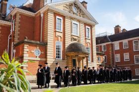 The Fellows of LMH, in black academic dress, congregate outside of Talbot Hall, an imposing red brick building