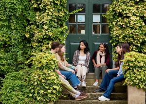 A group of students sitting on some steps outside of a red brick building covered in ivy