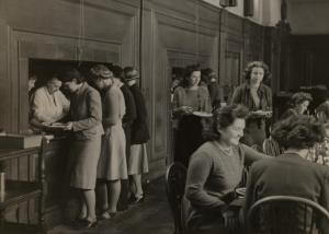A black and white archival photo of a group of Lady Margaret Hall students being served food in the Hall