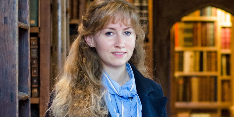 Cosima Gillhammer, a woman with long wavy blonde hair, stands in a library