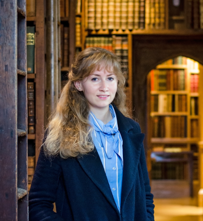 Cosima Gillhammer, a woman with long wavy blonde hair, stands in a library