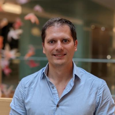 Oliver Pambos, who is wearing a pale blue shirt and standing in an atrium