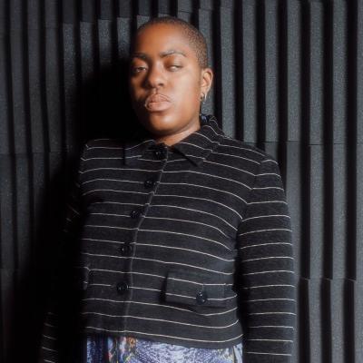 Onyeka Igwe, dressed in a black blazer and leaning against a black wall