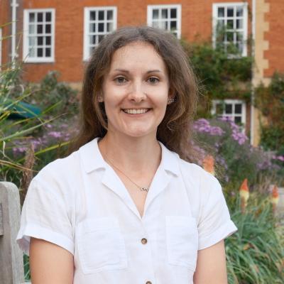 Dr Hannie Lawlor, a woman with long brown hair, sits on a bench in the LMH grounds